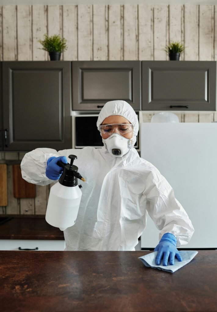 Person in protective gear disinfects kitchen counter with spray bottle.