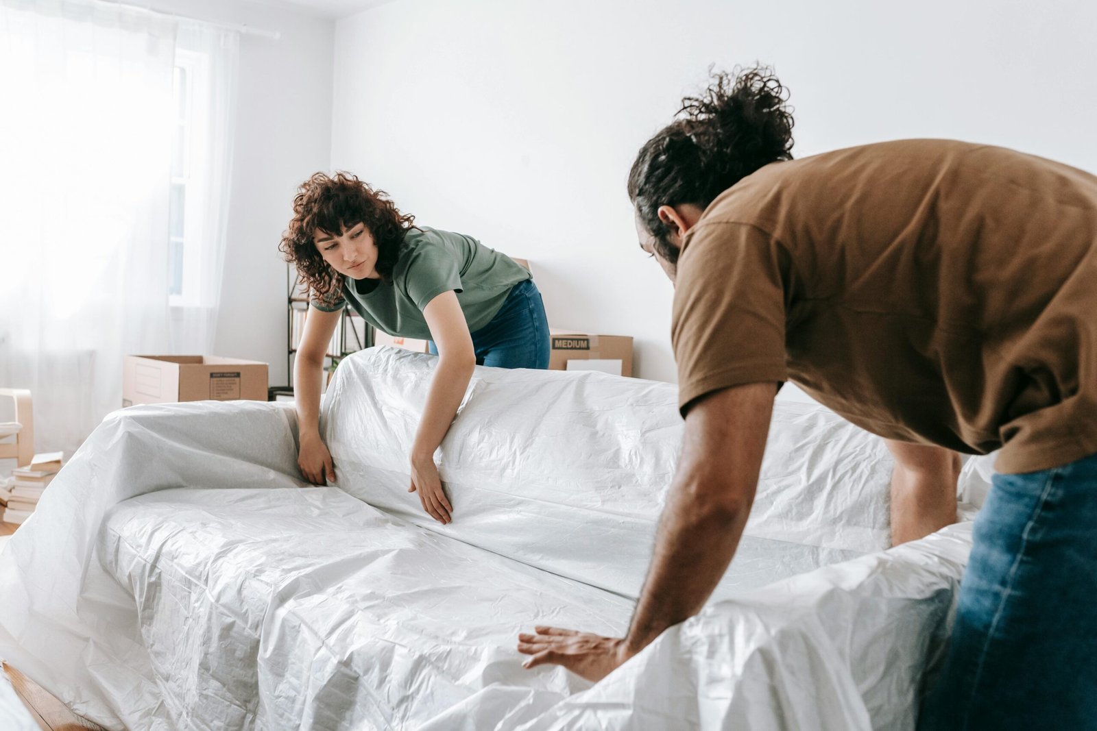 A couple wraps a sofa with white cloth while packing in their new apartment.